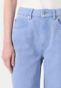 Svetlo modre jeans hlače z visokim pasom, ki imajo sprednje zapiranje na gumb, standardne žepke in diskretne šivanje podrobnosti.