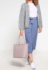 Jasnoszara, puszysta bomberka, biała koszulka, niebieskie kuloty i różowa torba na ramię ze złotymi elementami, w komplecie z białymi sneakersami.