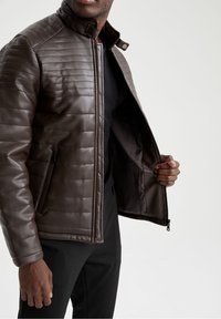 Giacca in pelle marrone trapuntata con collo alla coreana, chiusura frontale con zip e tasche laterali, con una fodera interna liscia.