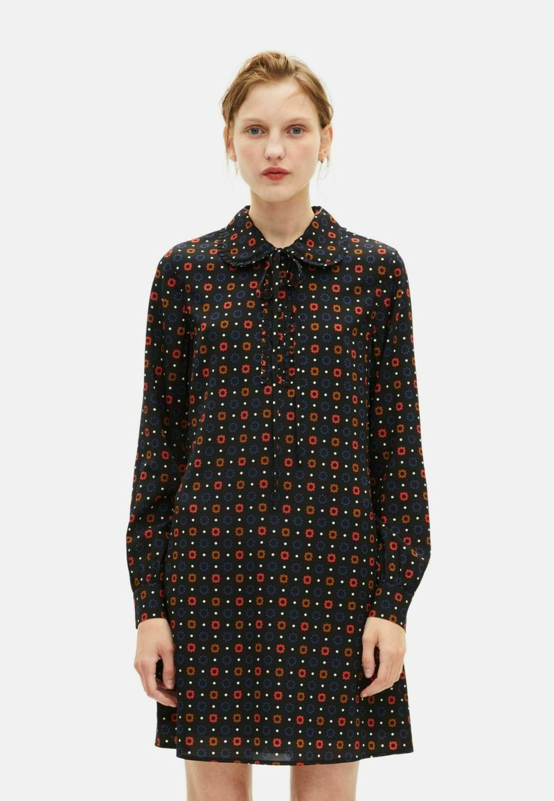 Czarna sukienka z długimi rękawami, kołnierzykiem i wiązaniem z przodu. Ozdobiona kolorowymi kwiatowymi wzorami, w prostym kroju i miękkiej teksturze materiału.