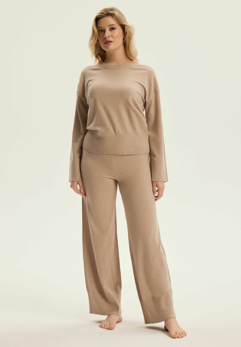 Beżowy dzianinowy komplet do relaksu, składający się z luźno dopasowanej bluzki z długim rękawem oraz spodni z szerokimi nogawkami i ściągaczami, prezentujący miękką fakturę oraz bezszwowy design.