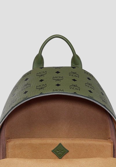 Zaino verde in pelle con un motivo texture e chiusura con zip. L'interno presenta un rivestimento in suede color cammello e una piccola etichetta in tessuto verde.