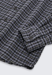 Camicia in flanella a trama a scacchi blu scuro e nera, con bottoni neri, polsini abbottonati e una consistenza morbida.