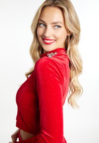Rode fluwelen top met lange mouwen en een cropped ontwerp, voorzien van sprankelende accenten en decoratieve knoopdetails op de schouder.
