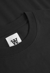 Zwarte t-shirt met een ronde hals van ribbelstof en een label met de merkinitialen in het wit op een rechthoekig etiket.