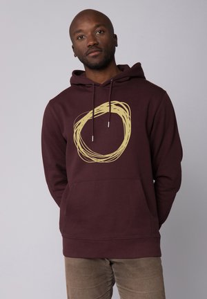 Maroon hoodie with a front pocket, featuring a beige circular graphic design. Made of soft fabric with drawstrings at the hood.