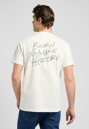 Cream cotton t-shirt featuring short sleeves and a round neck. The back displays bold gray text reading "BORN TO MAKE HISTORY."