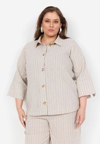Stribet blouse med spidse krave, trekvart ærmer og frontknapper. Stoffet er let med en beige bund og mørke striber.