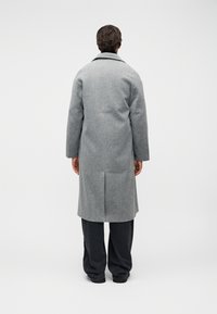 Γκρι μάλλινο παλτό με μεσαίο μήκος, με μία μόνο σχισμή στο πίσω μέρος και κλασικό γιακά, σε συνδυασμό με σκούρο παντελόνι.