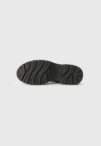 Suela de zapato de caucho negra con tracción texturizada y patrones de surcos, con el nombre de la marca grabado. Diseño plano adecuado para varios estilos de calzado.