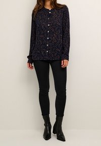 Chemise boutonnée bleu marine à motif paisley, tissu doux, manches longues et encolure ronde, associée à un jean skinny noir et des bottines.