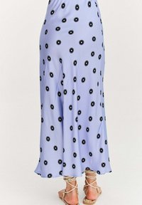 Levanduľové maxi šaty vyrobené z hladkej látky, zdobené čiernymi kvetinovými vzormi, s voľným strihom a s viazanými sandálmi na úrovni členku.