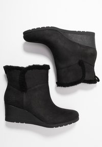 Botas de tobillo con cuña de ante negro y un acabado texturizado, con un borde de piel sintética en la parte superior. Cuenta con una suela de goma y el logo de UGG en el lateral.