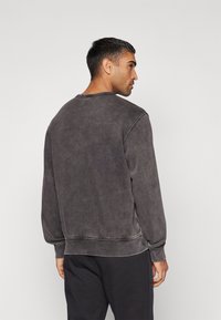 Dark gray sweatshirt with a relaxed fit, crew neck, and ribbed cuffs. Features a faded texture and visible stitching accents on the seams.