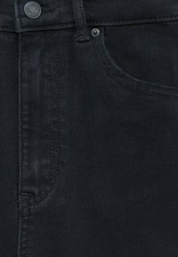 Gros plan sur un jean en denim noir montrant la poche avant, la boucle de ceinture, le bouton et les détails de couture visibles.