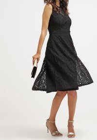 Černé krajkové šaty s přiléhavým korzetem, áčkovou sukní a délkou do kolen. V kombinaci se stříbrnými sandály na podpatku a černou kabelkou.