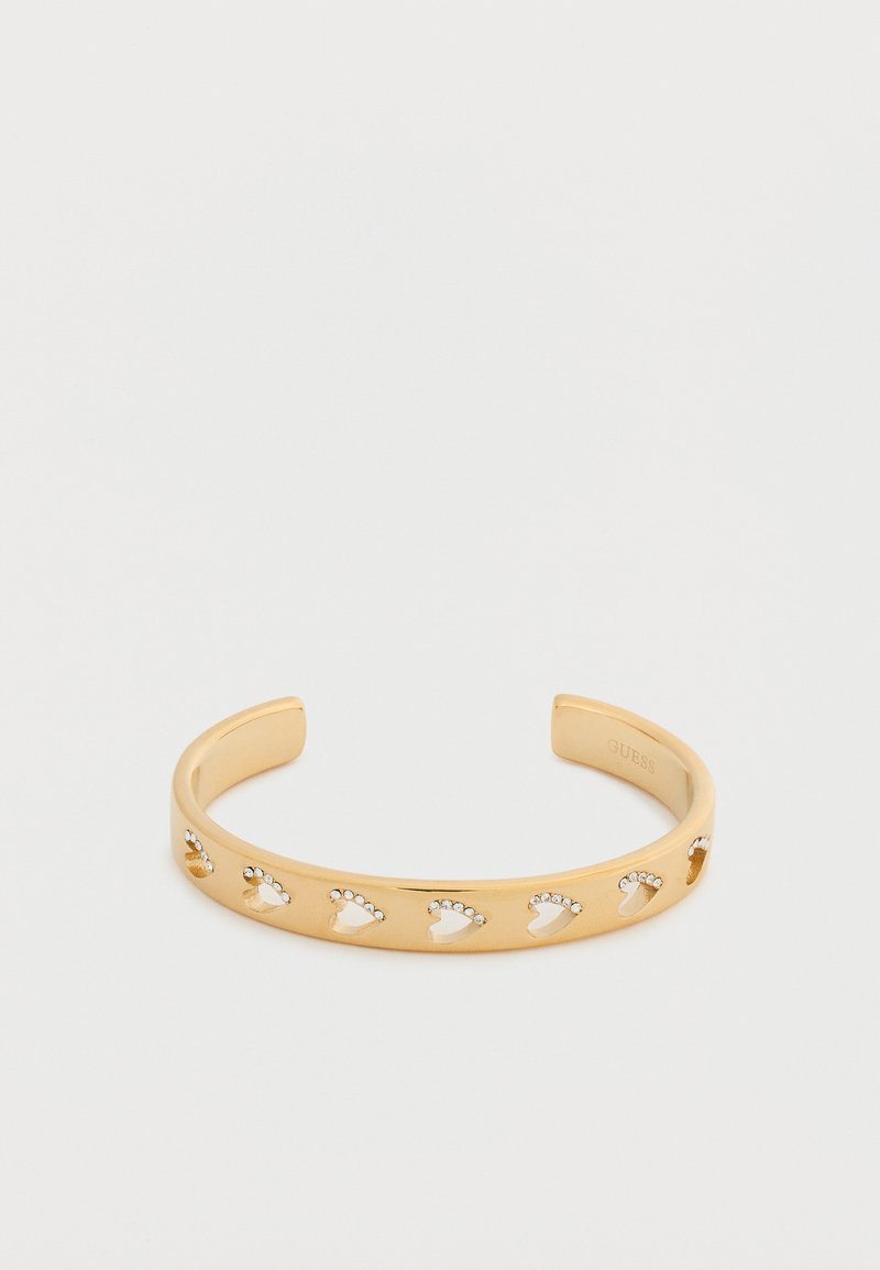 Βραχιόλι σε χρυσή απόχρωση με κοψίματα σε σχήμα καρδιάς, διακοσμημένο με μικρές στρας. Λείο φινίρισμα, ανοιχτό σχέδιο για ρυθμιζόμενο μέγεθος.