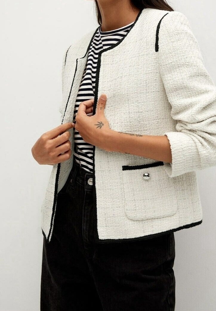 Veste en tweed blanche avec accents noirs, col rond et poches avant. Associée à une chemise rayée noire et blanche. Tissu texturé.