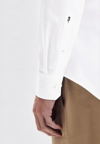 Camicia bianca a maniche lunghe, slim-fit, con polsini ricamati con un design di rose nere e chiusa con bottoni azzurro chiaro.