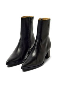 Botines de cuero negro con punta en forma de pico y tacón grueso. Cuentan con una cremallera lateral y una textura suave, con un brillo sutil.