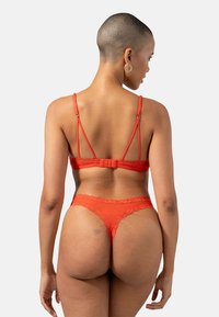 Ensemble de lingerie rouge avec des bordures en dentelle, des bretelles fines et ajustables, et une fermeture à crochets, mettant en valeur un design lisse et ajusté.
