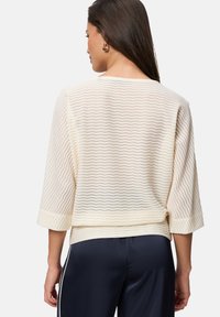 Haut en tricot crème à texture en zigzag avec des manches trois-quarts et une coupe décontractée, associé à un pantalon en satin bleu marine. Détails minimaux.