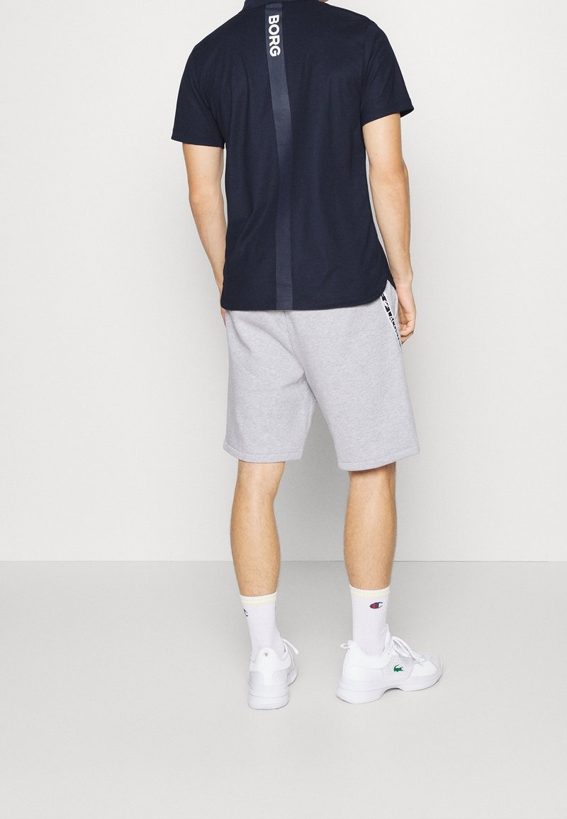 T-shirt bleu foncé à manches courtes avec logo BORG et short gris. Chaussettes blanches et baskets complètent la tenue décontractée. Design simple et sportif.