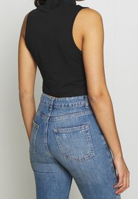 Svart ärmlös croppad topp med hög krage, kombinerad med blå högmidjade jeans som har bakfickor och en lätt sliten finish.