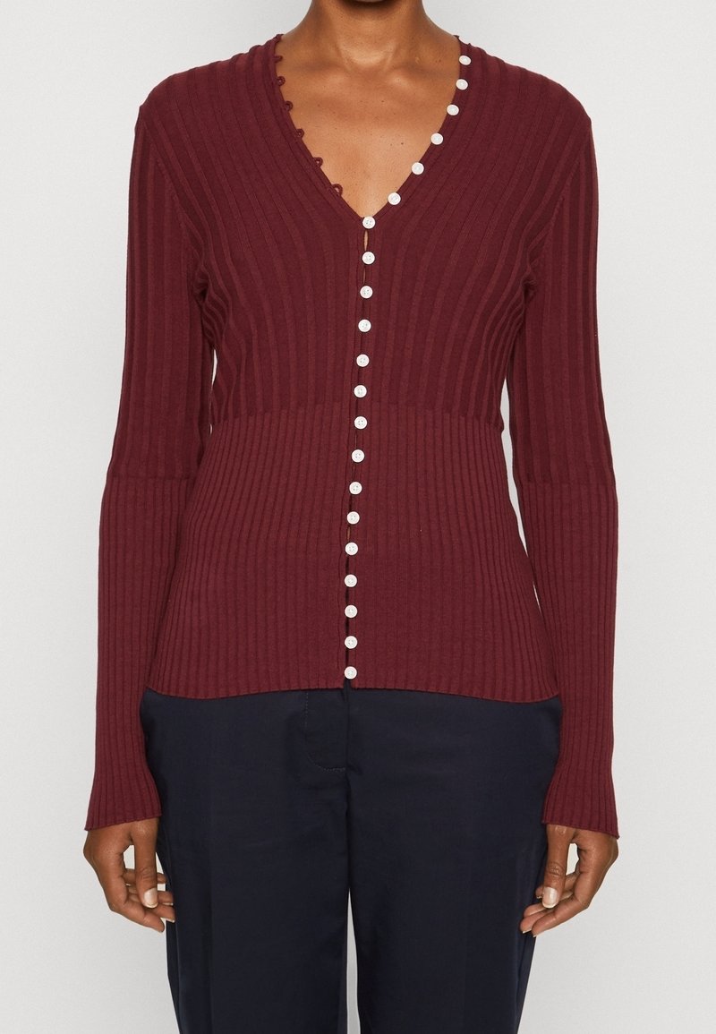 Viininpunainen resorineuloksinen neuletakki V-kaula-aukolla, jossa valkoiset napit edessä ja aaltoilevat reunat, pehmeästä neulosmateriaalista valmistettu.