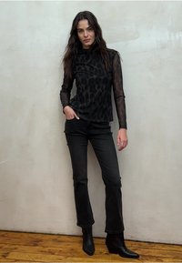 Zwarte top met lange mouwen en luipaardprint, gecombineerd met zwarte uitlopende jeans en puntige zwarte enkellaarsjes. Gestructureerde, semi-transparante mouwen.