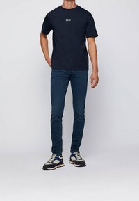 T-shirt en coton marine avec le logo "BOSS", associé à un jean bleu foncé et des baskets multicolores, présentant un mélange de textures et un design épuré.