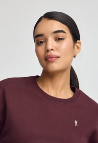 Felpa color bordeaux con scollo rotondo, caratterizzata da un piccolo logo bianco sul petto. Tessuto morbido e vestibilità classica.