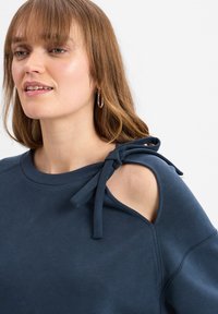 Marineblaue Sweatshirt mit kurzen Ärmeln, verfügt über seitliche Aussparungen und Bindebänder an der Schulter, hergestellt aus weichem, strukturiertem Stoff.