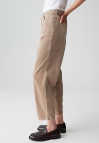 Pantaloni beige in cotone a gamba larga con vita alta, tasche laterali e posteriori e polsini, abbinati a mocassini marroni scuri.