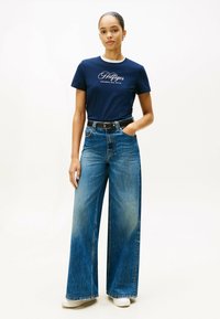 Marineblå bomulds t-shirt med hvidt logo, parret med højtaljede, brede blå jeans og hvide sneakers, med en bæltestrammende talje.