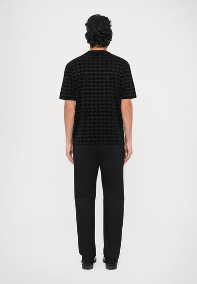 Čierne tričko s krátkym rukávom s geometrickým vzorom, skombinované s čiernymi rovnými nohavicami. Tkanina pôsobí mäkko a má textúrovaný povrch.