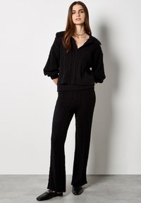 Conjunto de punto negro con un patrón de cable texturizado, cuello oversized y corte holgado. Complementado con zapatos negros planos.