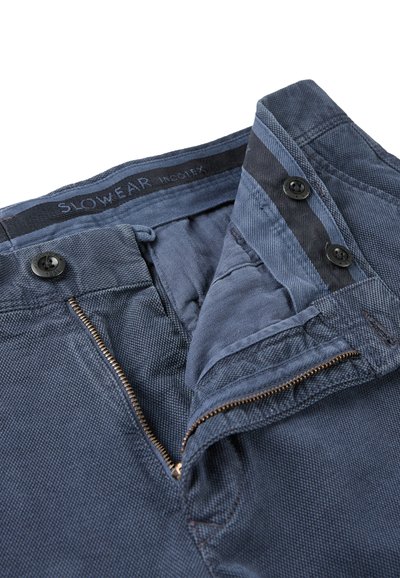 Granatowe spodnie bawełniane z zasuwakiem, zapięciem na guzik i wewnętrzną strukturą w jodełkę. Akcentowane kontrastowym, tkanym paskiem.