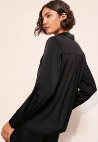 Sort langærmet bluse lavet af glat satin, med krave, knaplukninger ved håndleddene og en afslappet pasform med en detalje i form af en rygplissé.