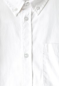 Camisa de botón blanca de algodón con cuello puntiagudo, botones y un bolsillo en el pecho. Textura suave sin patrones visibles.
