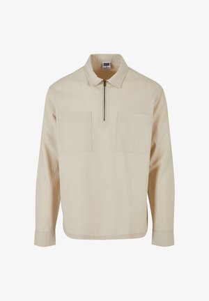 Beige Pullover-Oberteil aus strukturiertem Stoff, mit einem halben Reißverschluss, zwei Fronttaschen und langen Ärmeln mit geradem Saum.