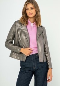Veste de motard en faux cuir gris métallique avec des détails matelassés, fermeture éclair inclinée et poches latérales, associée à un polo rose et un jean noir.