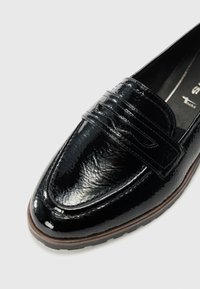 Črne patenten usnjene loafer čevlje z teksturirano površino, ki ima izrazit sedlo in rjavo gumijasto podplat. Kotna oblika prstov, eleganten profil.