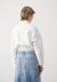 Kratka bela denimska jakna z ohlapnim krojem in elastičnim pasom, v kombinaciji s svetlo modro denimsko krilo z dvema hrtnima žepek.