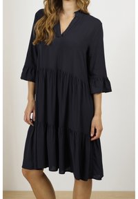 Navyblaues, kurzärmeliges Kleid mit V-Ausschnitt, schichtweisem Design und Rüschenbündchen. Hergestellt aus einem leichten, glatten Stoff.