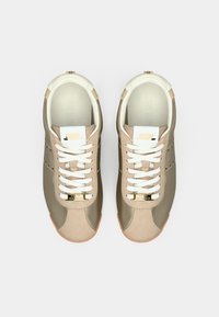 Μπεζ αθλητικά παπούτσια με λείο υφή, λευκά κορδόνια και χρυσές λεπτομέρειες. Διαθέτουν μαλακό γιακά και ελαστική εξωτερική σόλα για πρόσφυση.