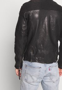 Giacca di pelle nera con accenti testurizzati sulle spalle e maniche a coste. Tasche con zip e vestibilità leggermente affusolata in vita.