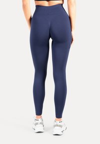 Marineblauwe leggings met hoge taille en textuur mesh accenten, voorzien van een zijzak en een gladde afwerking, gecombineerd met witte sportschoenen.