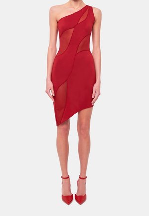 Femme portant une robe asymétrique rouge sans manches avec des panneaux courbes transparents, associée à des escarpins rouges à bout pointu avec bride à la cheville.