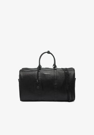 Zwarte leren duffeltas met dubbele handvatten, afneembare schouderriem en een bagagelabel, tegen een effen witte achtergrond.